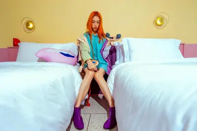 a woman with red hair sitting between two beds at The Fig Lobby Bangkok in Bangkok