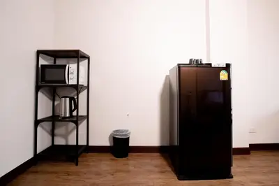 a black refrigerator next to a shelf with a microwave at Room 36 service apartment in Bangkok