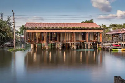 a building on the water next to a house at Humz Canal Stay in Nonthaburi