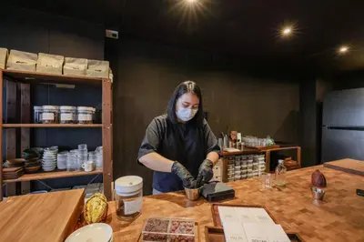 a woman in a mask preparing food on a table at Seekers Finders Rama IV Hotel SureStay Collection by BW in Bangkok