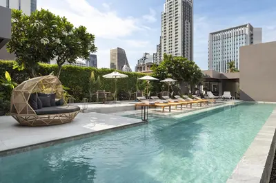 a swimming pool with chairs and tables and umbrellas at Ad Lib Hotel Bangkok in Bangkok
