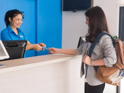a woman is handing a ticket to a woman at a counter at HOP INN Bangkok Krung Thonburi Station in Bangkok