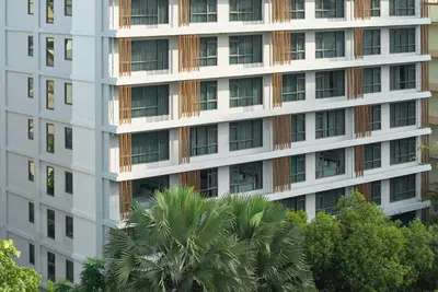 a tall white building with a palm tree in front of it at Livable Hotel Bangkok in Bangkok