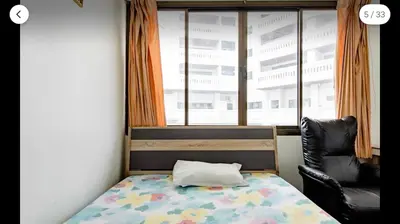a bedroom with a bed and a chair and a window at Flourish Apartments in Bangkok