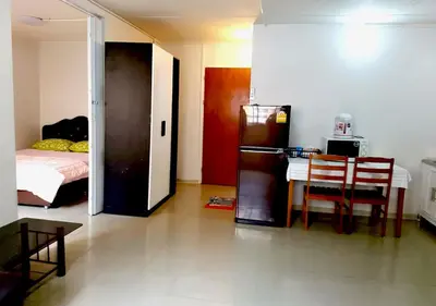 a room with a refrigerator and a table and a bed at ห้องใหญ่-ห้องพักรายวัน เมืองทองธานี เรือนศรีตรัง in Nonthaburi