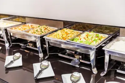 a buffet line with several trays of food and spoons at Livotel Hotel Lat Phrao Bangkok in Bangkok