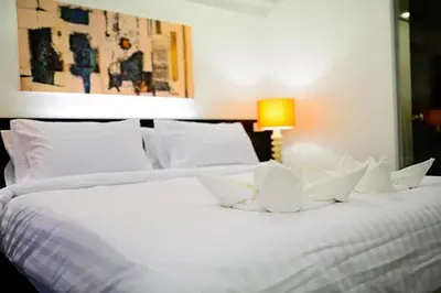 a white bed with white pillows and a lamp at UMA Residence in Bangkok