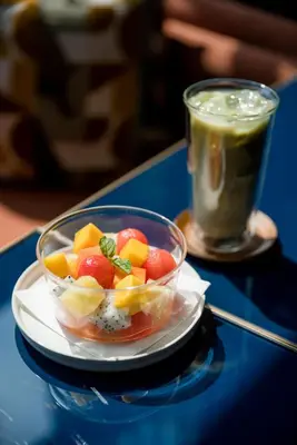 a bowl of fruit on a plate next to a drink at Public House Bangkok, a Member of Design Hotels in Bangkok