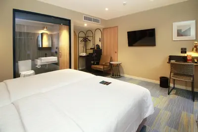 a hotel room with a large white bed and a bathroom at Benjarong Hotel Bangkok Ratchada in Bangkok