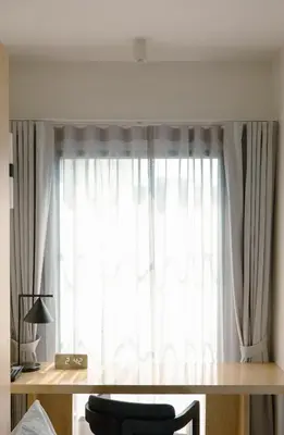 a window with white curtains and a desk with a chair at Hotel Sapin in Pom Prap