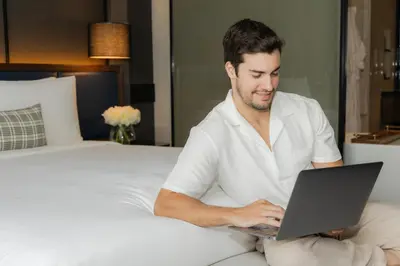 a man sitting on a bed using a laptop at InterContinental Bangkok Sukhumvit by IHG in Bangkok