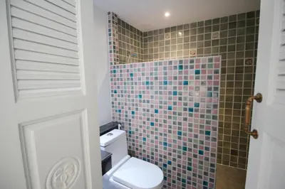 a bathroom with a toilet and a tiled wall at SASHA HOUSE in Ban Yang