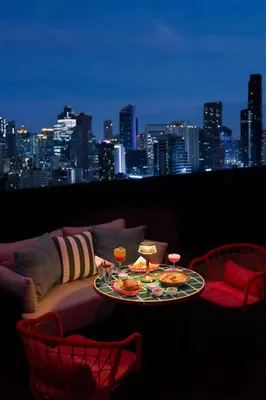 a table with food and drinks on a balcony with a city skyline at dusitD2 Samyan Bangkok in Bangkok