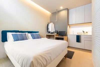 a bedroom with a large white bed and a kitchen at Silom Nara in Bangkok